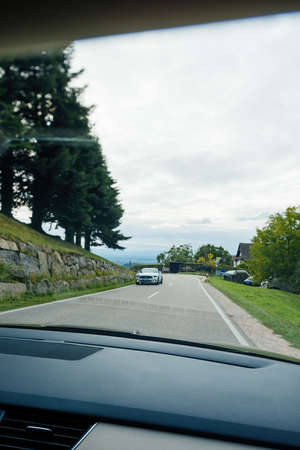 Switzerland - Sep 22, 2018: Driver POV at car view at the front driving Mustang Sport electric car - driving on rural highway surrounded by tall fir trees - tilt-shift photoのeditorial素材