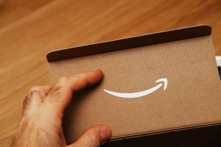 Paris, France, - Dec 18, 2020: Close-up male hand holding cardboard box with logotype of Amazon Company being cut in the cardboard panelのeditorial素材