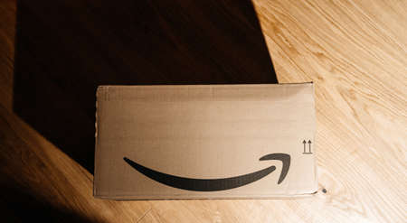 View from above of delivered Amazon Prime cardboard parcel - the company founded 30 years ago by Jeff Bezos - the long shadow of the box on the wooden floorのeditorial素材