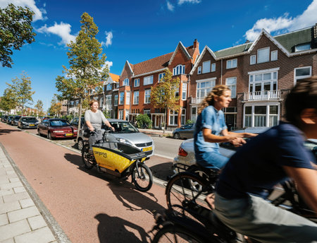 People riding bikes on Haarlem street with woman riding yellow shared Cargoroo e-cargo bike...