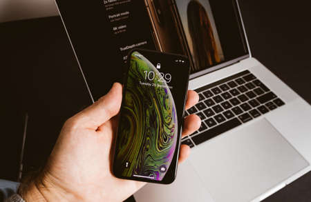 POV male hand holding latest Apple Computers Iphone Smartphone XS MAx telephone with date of THursday 25 September - the announcement of new latest smartphone - MacBook Pro laptop backgroundのeditorial素材