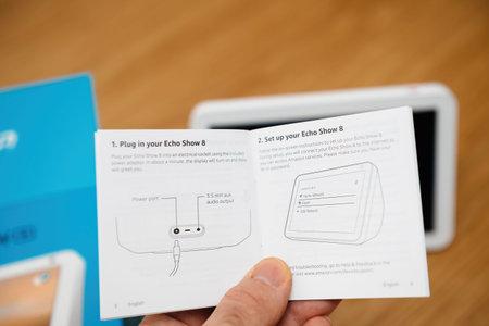 Male hand reading the instruciton manual of Amazon Echo Show 8 smart speaker device with Amazon...