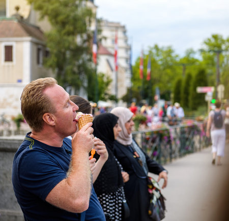 Adult male licking eating delicious ice-cream cone with women in background