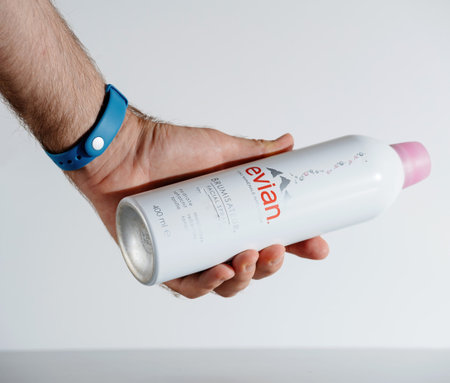 Male hand holding Evian Facial Spray bottle to be used on hot summer days