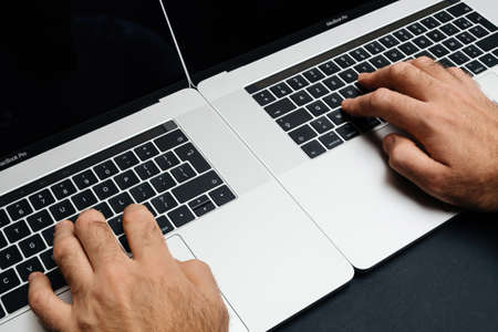 Male hand operating two laptop simultaneously professional Apple MacBook Pro 16のeditorial素材