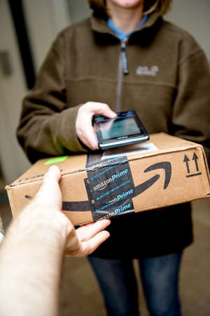 Male hand taking through the open door the cardboard parcel from Amazon Primeのeditorial素材