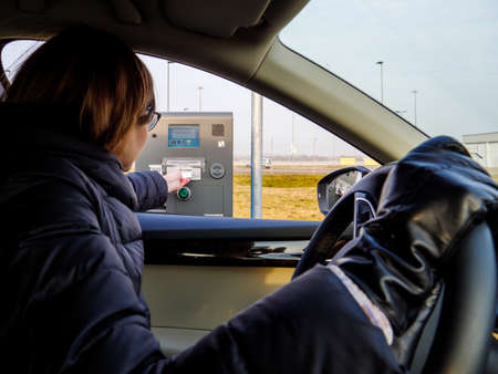 Side view of woman taking from the parking meter gate ticket to enter the security zoneのeditorial素材