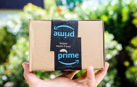 POV personal perspective male hand holding Amazon prime cardboard package carton box with free and fast delivery stickerのeditorial素材