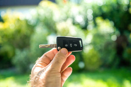 POV male hand holding new car key against green defocused backgroundの写真素材