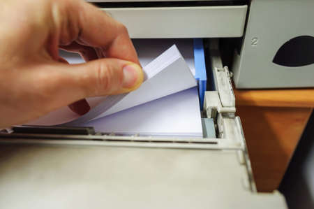 Male hand counting the stack of white paper in laser printerの写真素材