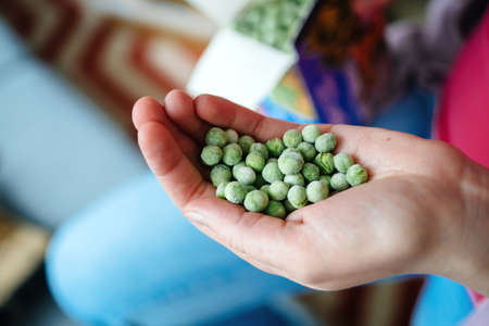 Side view of woman hand holding frozen peasの写真素材