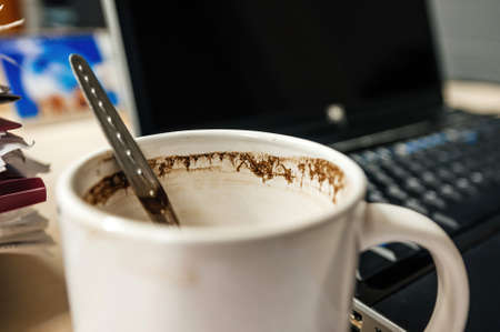 Cup of coffee with small spoon inside with open laptop lid in backgroundの写真素材