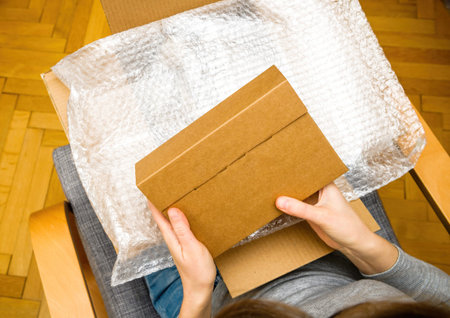 Overhead view of curious woman unboxing in the living room new silver package delivery