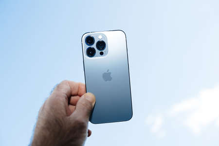 hand holding latest Apple Computers iPhone 13 pro with all three rear cameras and lidar sensor against blue skyのeditorial素材