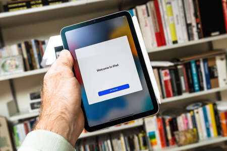 Books background male hand holding new ipad with Welcome get started button message on the new sixth-generation Apple Computers iPad Miniのeditorial素材