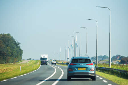 Rear view of Hyundai SUV, Mercedes truck driving fast on Dutch highway with led light poles and multiple wind turbines in backgroundのeditorial素材