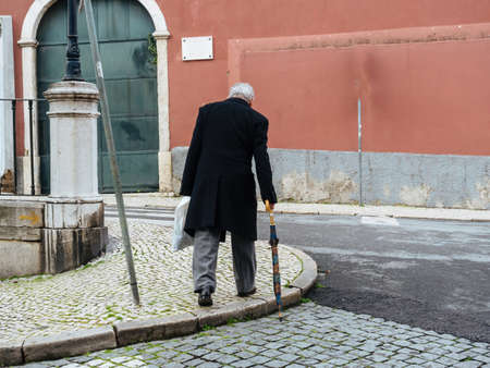 single senior man with cane walking on the cobblestone trottoir in central Lisbonの写真素材