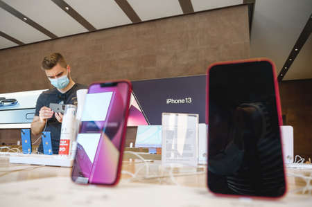 Curious adult customer wearing safety mask looking at the new Apple Computers iPhone 13 pro professional smartphone with multiple phones in foreground and alcohol gel in bottle due to covidのeditorial素材