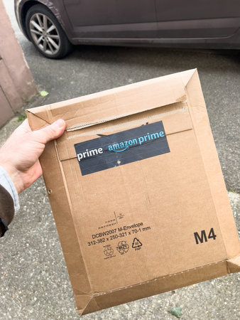 POV male hand holding package cardboard box with Amazon Prime logotype in front of his car- delivery...