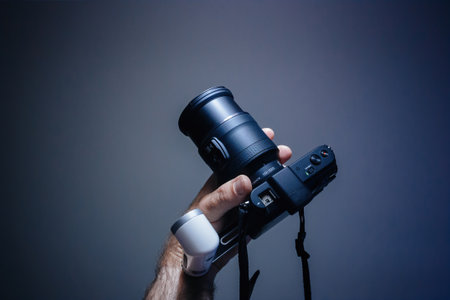 POv male hand holding new Nikon 1 NIKKOR 10-100mm f 4.5-5.6 VR camera lens for the on V1 mirrorless Nikon format against blue tech backgroundのeditorial素材