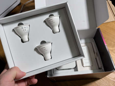 POV male hand unboxing set of new Philips Hue GU10 bulbs with white and color capabilities - smart illumination controlled by smartphones, computers and voice assistantsのeditorial素材