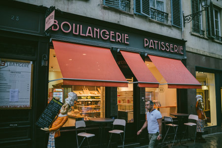 Lonely man walking in front of Bulagnerie patisserie with outdoor terrace in French city - rainy weatherのeditorial素材