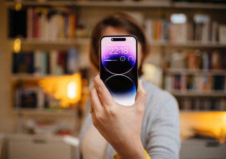 Woman holding Apple Computers iPhone 14 Pro Max in her hand with living room shelves in background