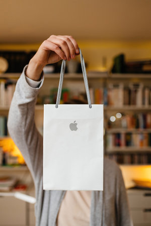 Woman holding Apple Computers gift paper shopping bag in front of her with living room shelves in backgroundのeditorial素材