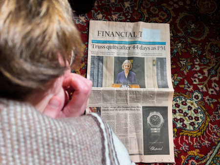 View from above of woman reading in living room floor the front page of Financial Times announcing...