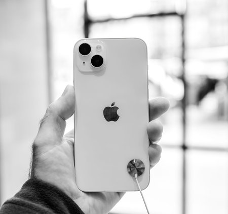 Male hand holding new powerful gold colored iPhone 14 Plus new smartphone by Apple Computers rear...
