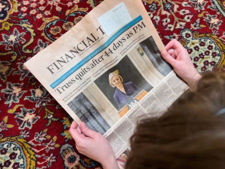 Directly above view of woman reading on the living room silk rug floor latest Financial Times with headline Liz Truss quits after 44 days as British Prime-ministerのeditorial素材