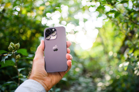 Man holding new Deep purple Apple Computers iphone 14 pro smartphone with green defocused cherry...