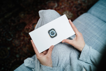 POV woman hand holding the package showing new Apple Watch Series Ultra designed for extreme activities like endurance sports - living room sofaのeditorial素材