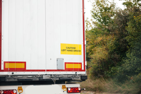 Caution, left hand driver signage on a white cargo truck driving