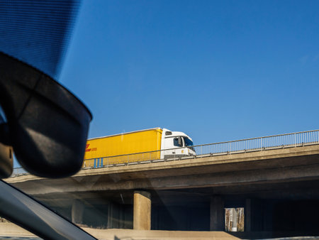 yellow fast DHL truck driving on a bridge above autobahn - low angle view from a carのeditorial素材