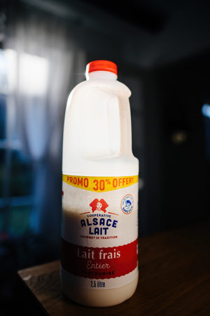 Whole milk white bottle with logotype of Alsace Lait on a wooden table with light illuminating the...