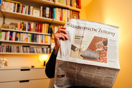Woman reading in her living room latest German newspaper featuring on front page breaking news of UBS historic acquisition of rival Credit Suisse Group AG - Vitsoe 606 shelves in backgroundのeditorial素材