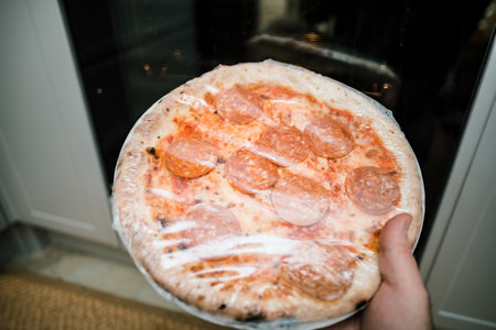 POV male hand holding deep frozen pizza with salami in handの写真素材