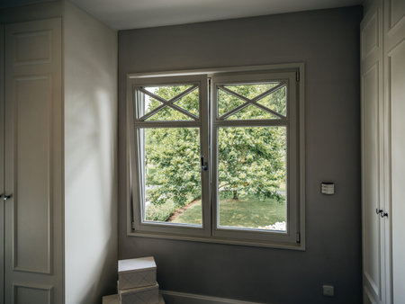 An inviting bedroom scene with a window framing the verdant outdoors, casting shadows that play with...