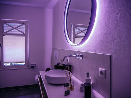 An intimate bathroom setting bathed in a violet hue, featuring a striking LED-lit mirror, blending functionality with modern aesthetic touches.の写真素材