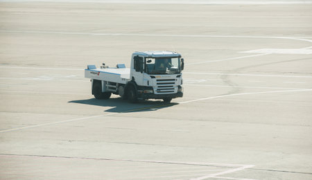 Frankfurt, Germany - Oct 2, 2015: A Scania airport tug vehicle by Swissport drives on the tarmac, its cargo services empty, under the bright glare of the sun.のeditorial素材