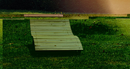 A wooden bench sits peacefully on the lush, green field, offering a tranquil spot for relaxation and contemplation light flare on rightの写真素材