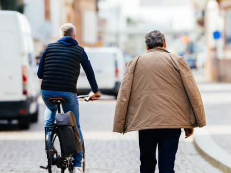 Rear view of an elderly person walks alongside a cyclist on a quiet urban street, enveloped by the crisp vibe of fall.の写真素材