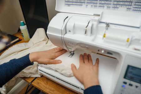 Elegant woman hands carefully guide fabric through a sewing machine, focusing on the detailed...
