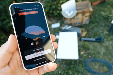 Germany - Jun 15, 2023: Hand holding a smartphone displaying estimated obstructions for a Starlink setup with equipment and cables visible in the outdoor background.のeditorial素材