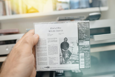 Paris, France - Jun 3, 2024: POV of a male hand holding a luxury numbered copy of a Japan pressing SACD disk of Miles Davis Kind of Blue, with a luxury SACD player with an open tray and an impressive amplifier in the background.のeditorial素材