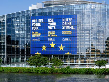 Strasbourg, France - Jun 6, 2024: Close-up of the European Parliament building in Strasbourg featuring a large banner in multiple languages encouraging voting in the 2024 EU elections, with reflections on the glass facade and a river in the foreground.のeditorial素材