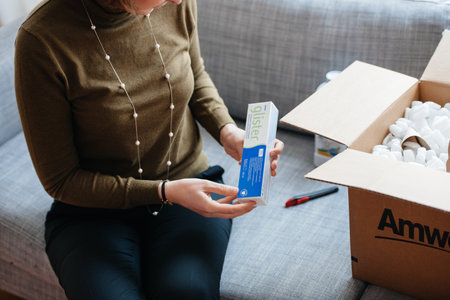 Paris, France - Oct 20, 2015: Woman unboxing a tube of Glister toothpaste from an Amway box, sitting on a grey couch, examining the product while unpackingのeditorial素材