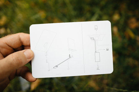 Frankfurt, Germany - Jun 15, 2023: Close-up of a hand holding the installation guide for a Starlink Ethernet adapter, with detailed diagrams, set against a blurred grassy backgroundのeditorial素材