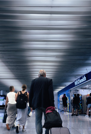 Palma, Spain - Jul 11, 2024: Back view of travelers walking through an airport terminal, with a WHSmith store visible to the side and a man pulling a suitcase, emphasizing the busy airport environmentのeditorial素材